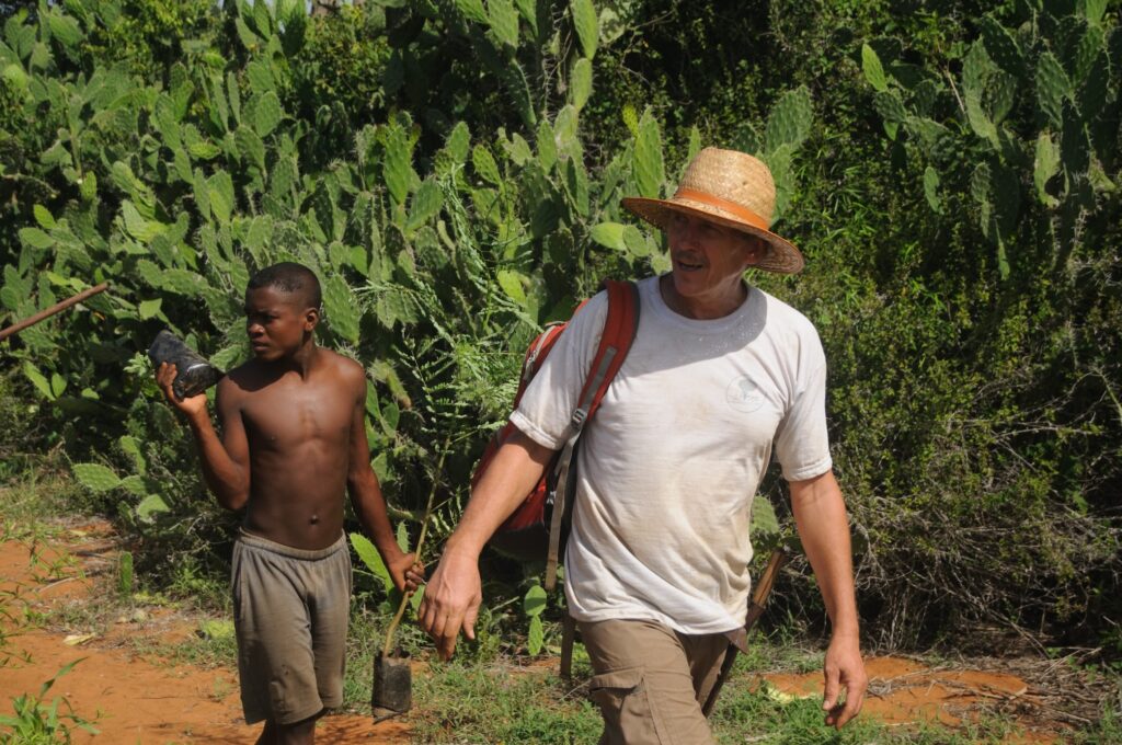 Joachim Milz walking beside a young boy carrying seedlings during a mission in Kenya